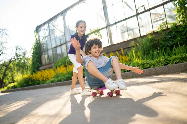 Smiling joyous young lady supporting a boy during skateboarding — Foto Stock