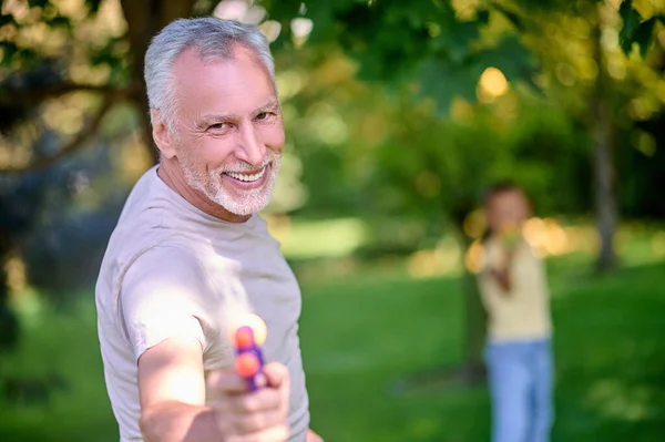 Mature gray-haired man playing paintball with a girl — ストック写真
