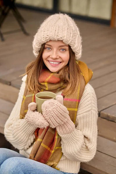 Žena s kávou sedí na verandě a dívá se do kamery — Stock fotografie