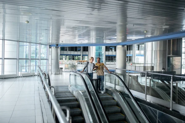 Turistas concentrados examinando un documento de viaje en la escalera mecánica del aeropuerto — Foto de Stock