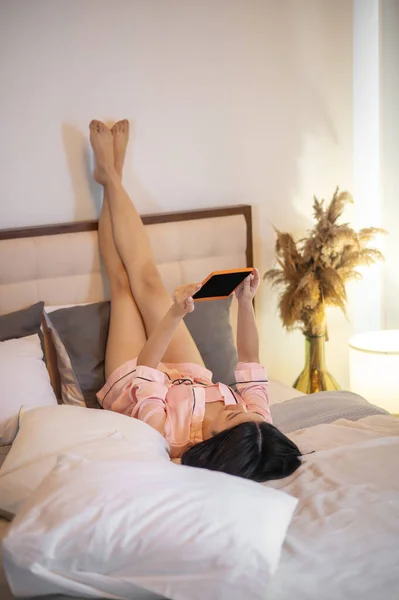 Donna sdraiata con le gambe sollevate guardando tablet — Foto Stock