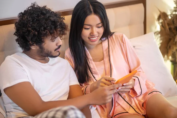 Man and woman interestedly looking at tablet on bed — Stockfoto