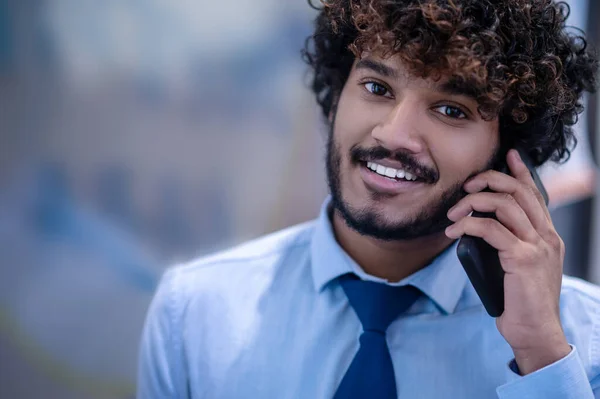 Curly-haired young businessman in a blue shirt talking on the phone — стоковое фото