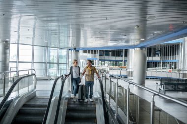 İki yolcu hareket halindeki merdivenlerden aşağı iniyor.