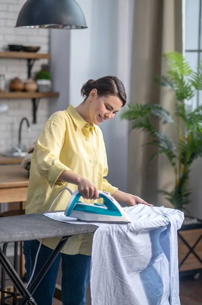 Mujer alegre planchando ropa arrugada en la tabla de planchar — Foto de Stock