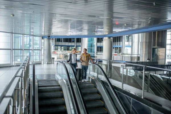 Dos pasajeros del aeropuerto conversando en la escalera mecánica — Foto de Stock
