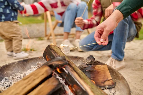 Male hand holding marshmallows on skewer over bonfire — Stock Photo, Image