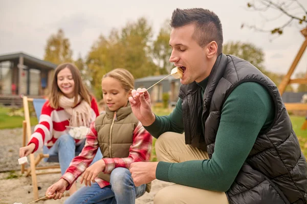 Hombre con los ojos cerrados mordiendo malvaviscos en el picnic — Foto de Stock