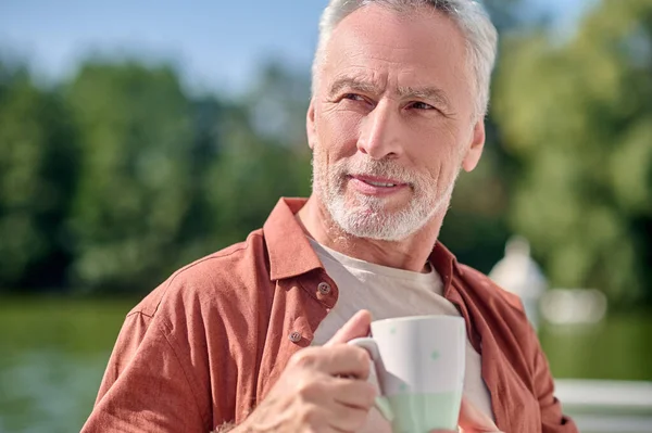 A mature bearded man with a cup in hands — Stockfoto
