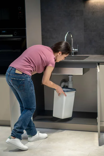 Mujer poniendo cubo bajo el fregadero con fugas — Foto de Stock