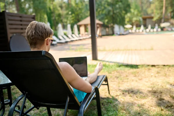 A man sitting on a chaise longue and working on a laptop — Fotografia de Stock