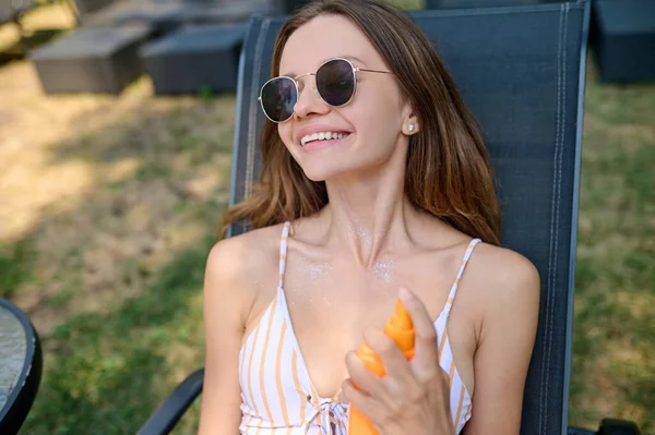 Mujer joven rociando crema spf en su cuerpo —  Fotos de Stock