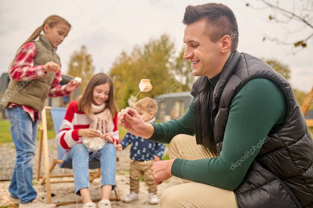 Man squatting sideways to camera looking at marshmallows