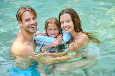 Cute girl and her parents spending time at the swimming pool
