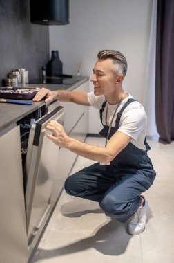 Man crouched peeking into crack door of washing machine