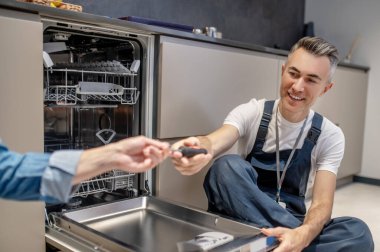 Hand holding out tool to plumber sitting on floor