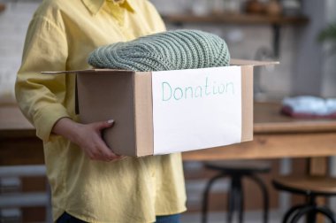 Caucasian lady showing a cardboard box with folded clothes