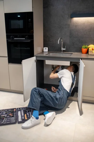 Чоловік сидить, дивлячись під кухонну раковину — стокове фото