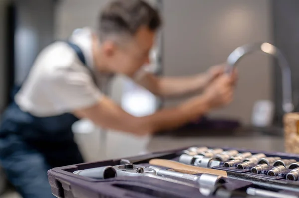 Tools in open case and man repairing water tap — Stockfoto