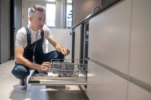 Man crouching down opening dishwasher inspecting