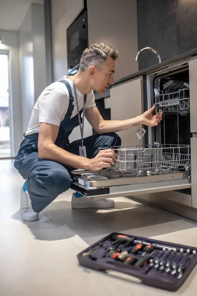 Profile of man crouching looking into open dishwasher — Stock Photo, Image