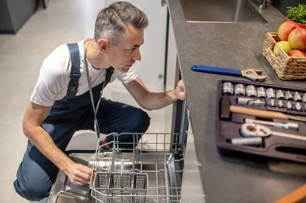 Man sitting near an open dishwasher and tools — Stockfoto