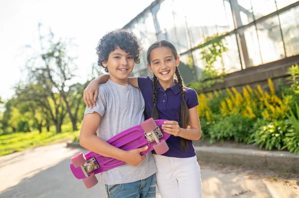 Joyous young lady embracing her friend skateboarder — Photo