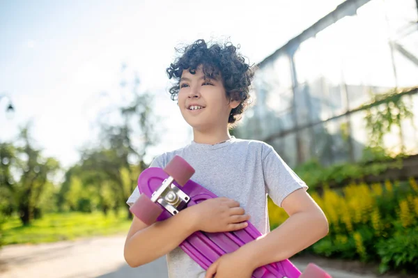 Cute kid with the skateboard in his hands standing outdoors