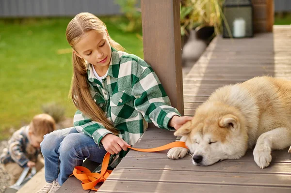 Girl sitting on porch looking touching lying dog — Photo
