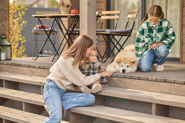 Woman with child and girl looking at lying dog — Photo