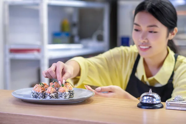 Asian woman putting sushi on the plate and looking inspired — Stock Photo, Image