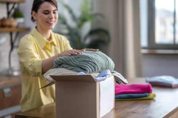 Señora feliz colocando suéteres en el cartón — Foto de Stock