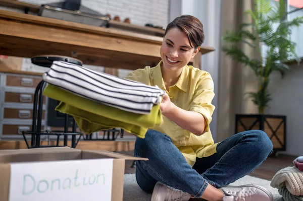 Joyous volunteer seated on the floor packing clothes for donation — Foto Stock