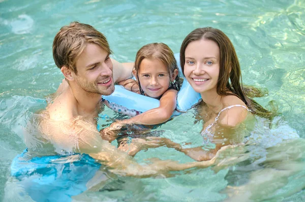 Cute girl and her parents spending time at the swimming pool Stock Picture