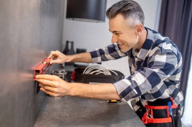 Man touching measuring device to wall near power socket