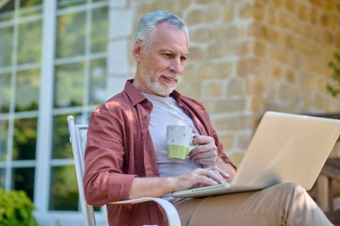 A man in burgundy shirt with a laptop in hands