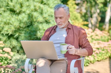 A man in burgundy shirt with a laptop in hands
