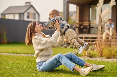 Woman sitting on lawn raising up child