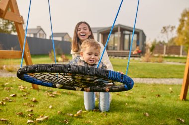 Child on swing and woman kneeling on lawn
