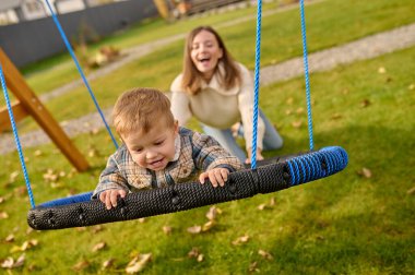 Woman pushing swing with joyful child