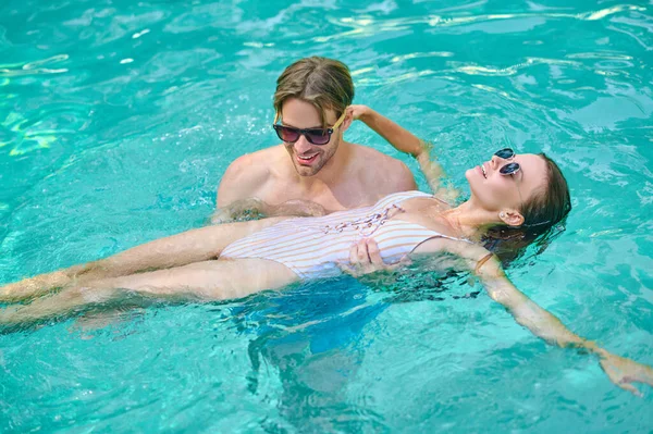 Young woman laying on water and looking relaxed, her man holding her — Stock Photo, Image