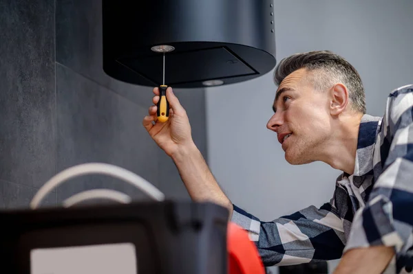 Man with screwdriver twists lamp on kitchen hood — Stockfoto