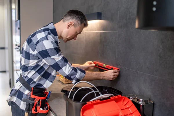 Man sideways to camera applying measuring device to wall — Stock Photo, Image