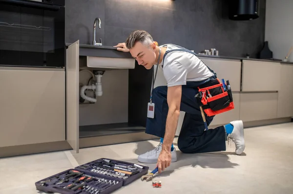 Man crouched near sink stretching out hand to wrench — Stock Photo, Image