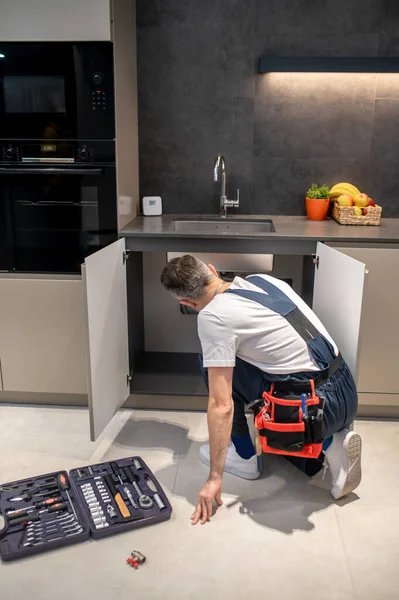 Back view of man crouching near kitchen sink — 스톡 사진