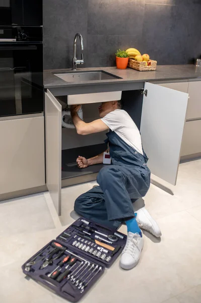 Man with tools peeking under kitchen sink — Stockfoto