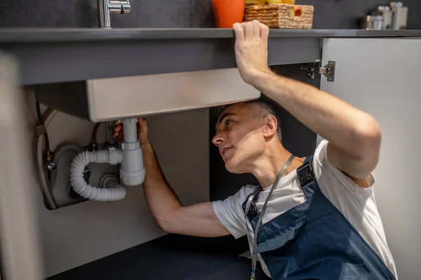 Man carefully examining bottom of sink and pipe — Zdjęcie stockowe