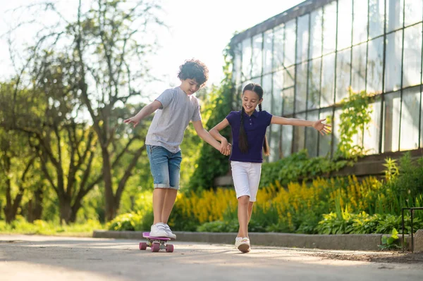 Boy learning to ride the skateboard aided by a girl — Φωτογραφία Αρχείου