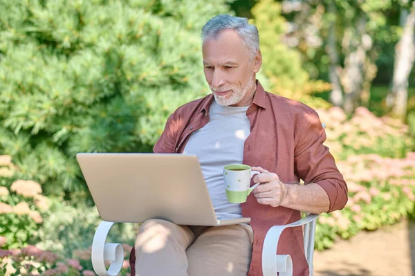 Ένας άνδρας σε μπορντό πουκάμισο με ένα φορητό υπολογιστή στα χέρια — Φωτογραφία Αρχείου