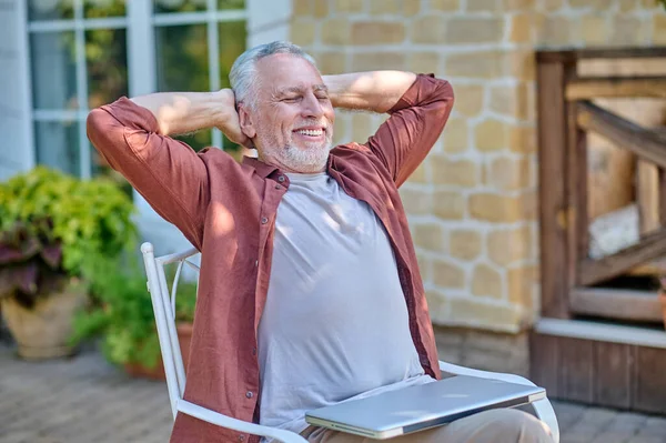 Gray-haired mature man sitting in a armchair and stretching — Stock Photo, Image
